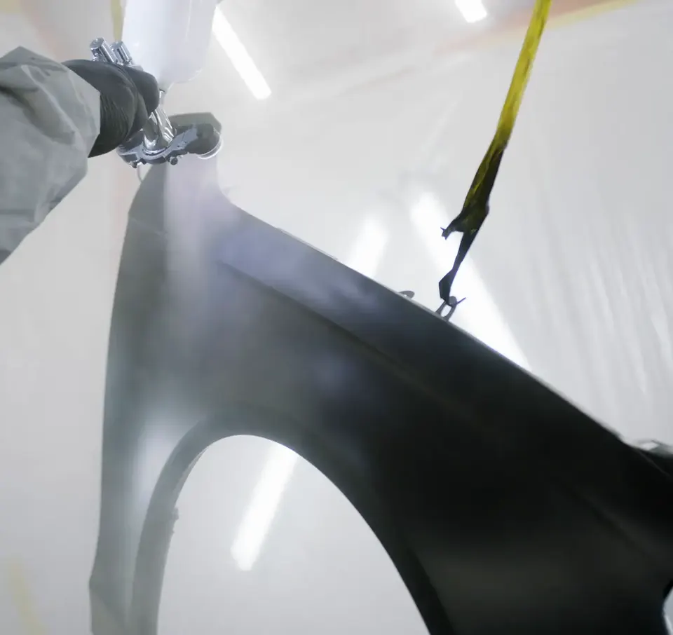 Close-up of a spray gun applying paint to a car panel in a spray booth